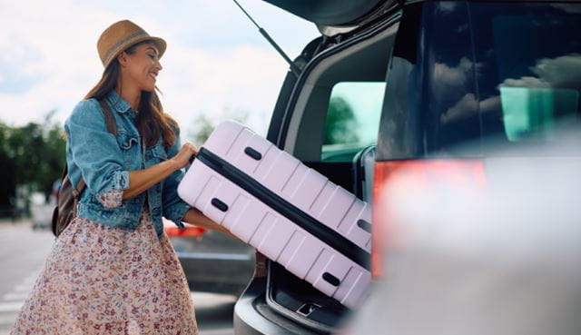 Person on holiday loading suitcase in to car boot